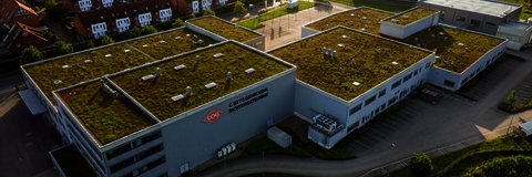 COG Firmengebäude in Pinneberg Luftbild des COG Unternehmensstandorts in Pinneberg: moderne Produktionsgebäude mit nachhaltigen Gründächern, eingebettet in eine grüne Umgebung mit Wohnhäusern und Infrastruktur.